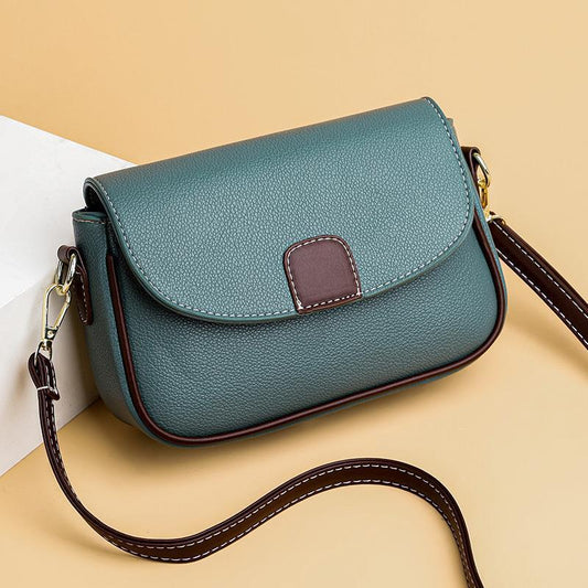 Teal handbag with a brown strap on a beige background